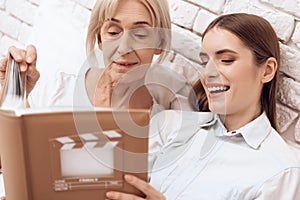 Girl is nursing elderly woman at home. They are watching photos in photo album.