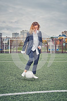 Girl in an office suit hitting hitting soccer ball on the stadium field. concept