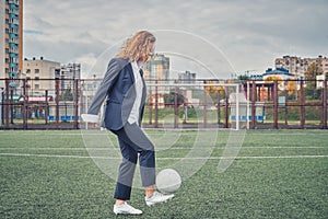 Girl in an office suit hitting hitting soccer ball on the stadium field. concept