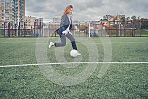 Girl in an office suit hitting hitting soccer ball on the stadium field. concept