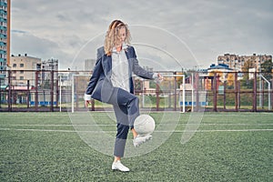 Girl in an office suit hitting hitting soccer ball on the stadium field. concept