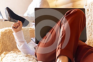 Girl in office uniform lying on sofa with shoes in her hand and laptop.
