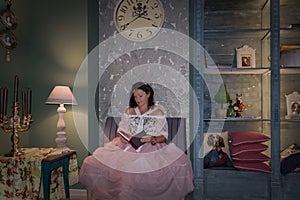 A girl in an old-fashioned pink dress is reading a book
