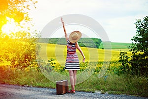 Girl with old suitcase standing on roadside in sun