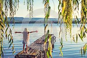 Girl on a old wooden fishing pier and willow tree enjoying beautiful sunset over the sea lake