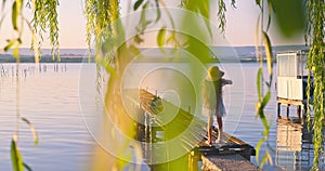 Girl on a old wooden fishing pier and  willow tree enjoying beautiful sunset over the sea lake, 4K nature landscape video