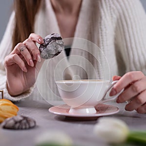 The girl in one hand holds a chocolate cookie in the other cup of cappuccino on the table. Coffee break with sweet.