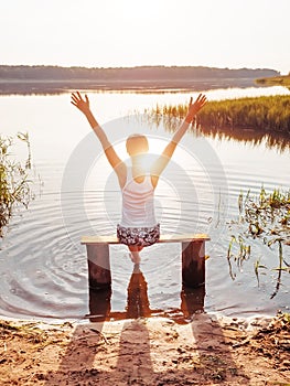 Girl with open hands. Woman arms raised up. The girl sits on a bench by the river and enjoys a beautiful sunset. Girl