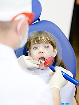 Girl with open mouth receiving dental filling dryi