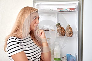 Girl opened the refrigerator and thinks what to eat