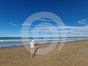 Girl opening her arms in front of the sea with a seagull flying in front of her.