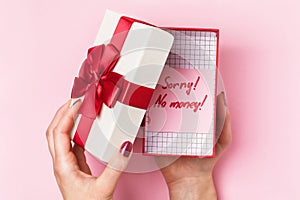 Girl opens a box with a gift on a pink background, top view. Concept no money for gifts