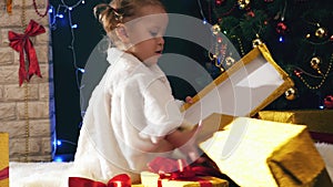 Girl opens Christmas gifts boxes near fireplace, decorated Cristmas tree