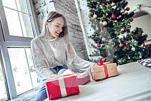 Girl opens a gift against the background of the Christmas tree. happy young woman celebrating Christmas