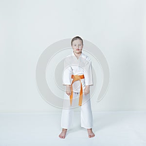 A girl with an orange belt is standing in a karate stand