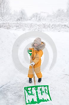Girl in orange jumpsuit cleans snow big shovel.
