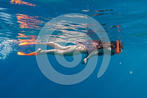 Girl in orange swimming mask and flippers dive in deep sea