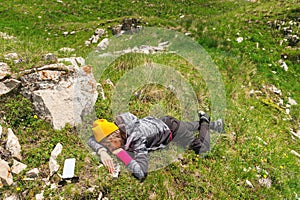 Girl outdoors sleeping on the green grass against a stone in nature. Perishing and fatigue in nature