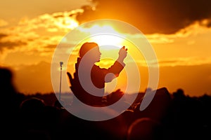 Girl over the crowd against the sunset sky. Having fun and using her smartphone at the summer festival