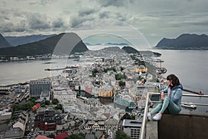 Girl overlooking the coastline of city Alesund with colorful houses and mountains in Norway