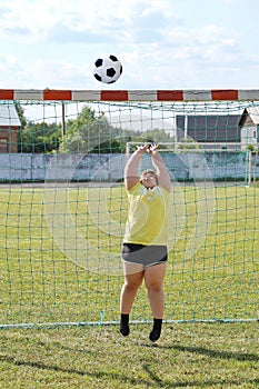 Girl with overweight stands in football gate and jumps to catch ball with his hands