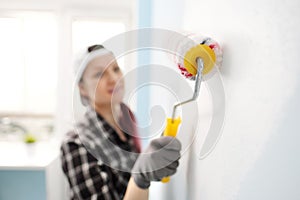 Girl painter, designer and worker paints a roller and brush the wall. Smiling, working with pleasure, close-up.