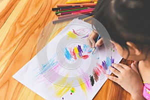 Girl painting on paper sheet with colour pencils on the wooden table at home - child kid doing drawing picture and colorful crayon