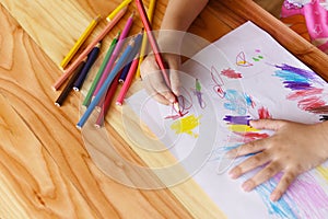 Girl painting on paper sheet with colour pencils on the wooden table at home - child kid doing drawing picture and colorful crayon