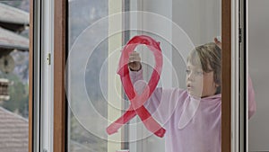 Girl is painting red ribbon on the glass of the window