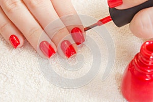 Girl paints her nails red nail polish. Beauty salon. manicured hand on white towel and red bottle gel laquer