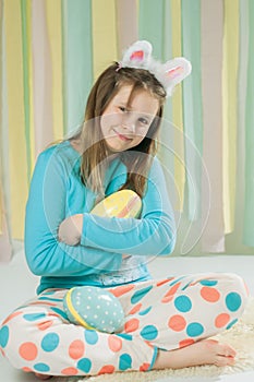 A girl in pajamas with a easter eggs sitting on the floor