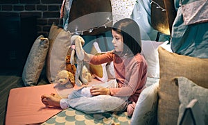 Girl in pajamas playing alone with teddies in a play shelter