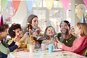 Girl With Parents And Friends At Home Celebrating Birthday Firing Confetti Poppers At Party