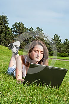 Girl in park lies on grass and work with laptop.