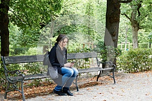 A girl in the park sits alone on a bench with a phone