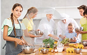 Girl participant in culinary master class is standing with bowl in hands.