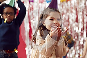 Girl In Party Hat Celebrating At Birthday Party Blowing Handful Of Gold Confetti And Glitter