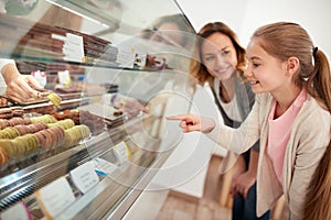 Girl in pastry shop select macarons from showcase