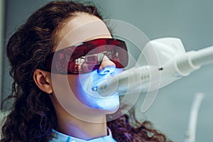 Girl patient in the dental clinic. Teeth whitening UV lamp with photopolymer composition