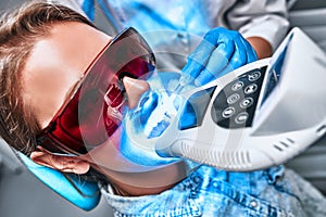 Girl patient in the dental clinic. Teeth whitening UV lamp with photopolymer composition