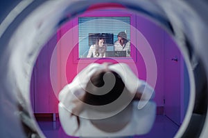 The girl patient is lying in the tomograph and waiting for a scan. Three doctors from the exam room look at the pictures