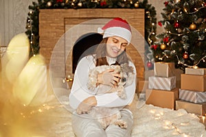 Girl with Pekingese dog on background of Christmas decorations and fireplace, woman with puppy sitting on floor on soft carpet,