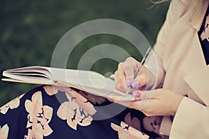 girl with pen writing on notebook on grass outside.