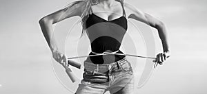 Girl with perfect waist with a jump rope in hands. Athletic slim woman measuring her waist by measure tape after diet