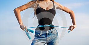 Girl with perfect waist with a jump rope in hands. Fit fitness girl measuring her waistline with measure tape. Athletic