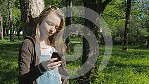 Girl with a phone in the park. A teenage girl in the fresh air with a mobile. Beautiful girl with freckles.