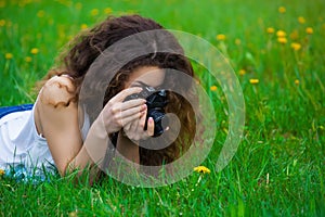 Girl-photographer with curly hair lying on the grass in the park, holding a camera and photographed the flower.