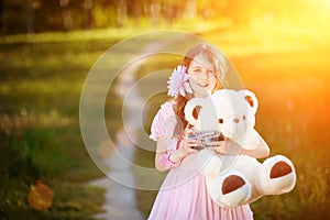 The girl-photographer in a pink dress hugging a teddy bearin the rays of a bright sun