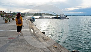 Girl photographer Standing alone on the docked sailboat in the sunny harbor, a charming lady in a jacket enjoys the summer coast