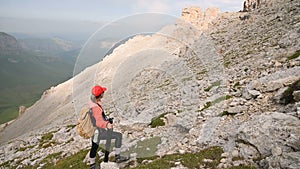 A girl photographer stands resting from a climb on a mountainside against the backdrop of cliffs of a plateau and the